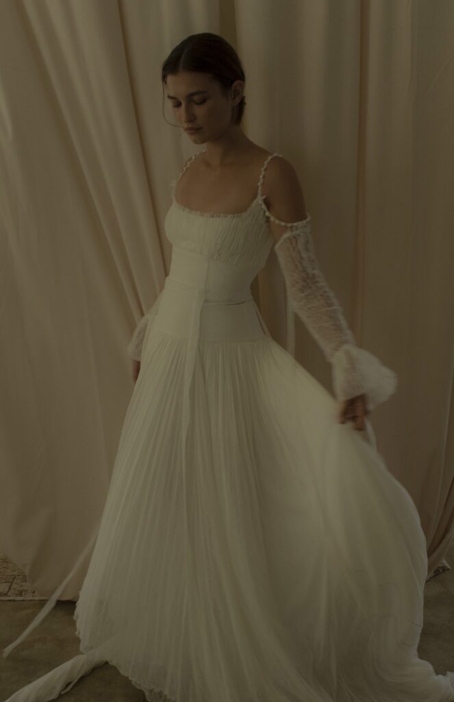 Cinq's wedding dress designs give a vintage feeling while being modern and timeless. This long wedding gown is off the shoulder, with two pearl straps.